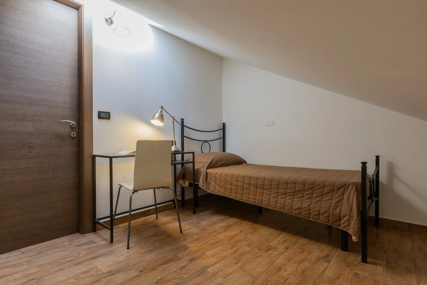 A bedroom with a single bed, desk, and chair beneath a sloped ceiling.
