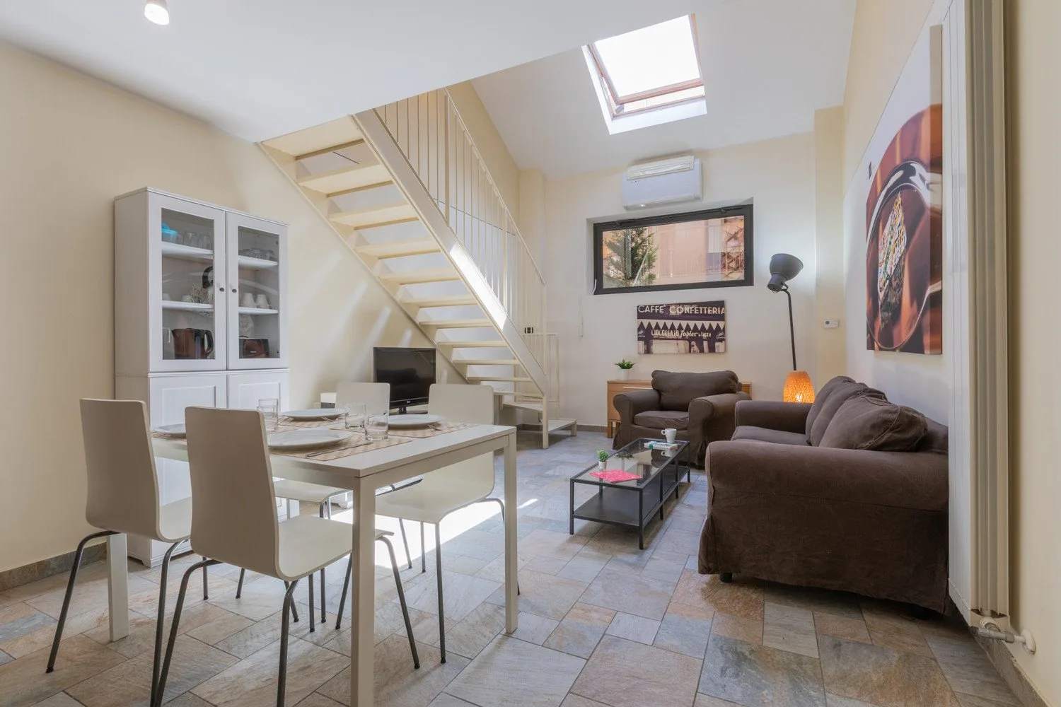A combined living and dining room with a staircase and skylight.