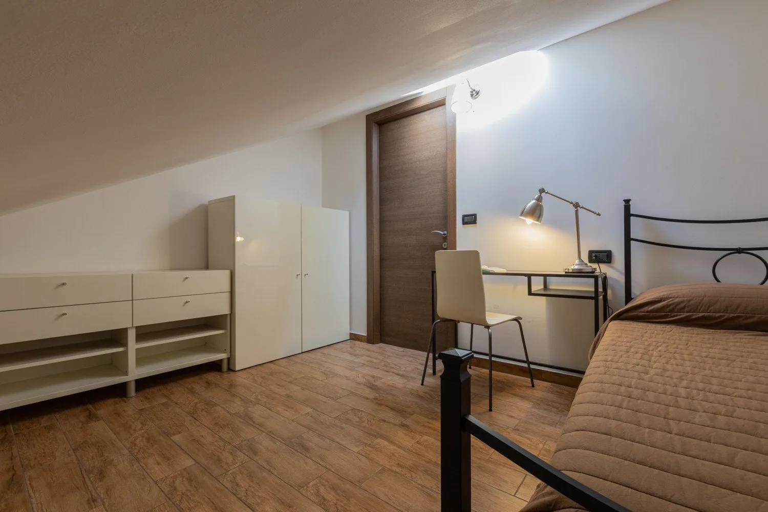 Un dormitorio con cama, escritorio y armarios bajo un techo inclinado.