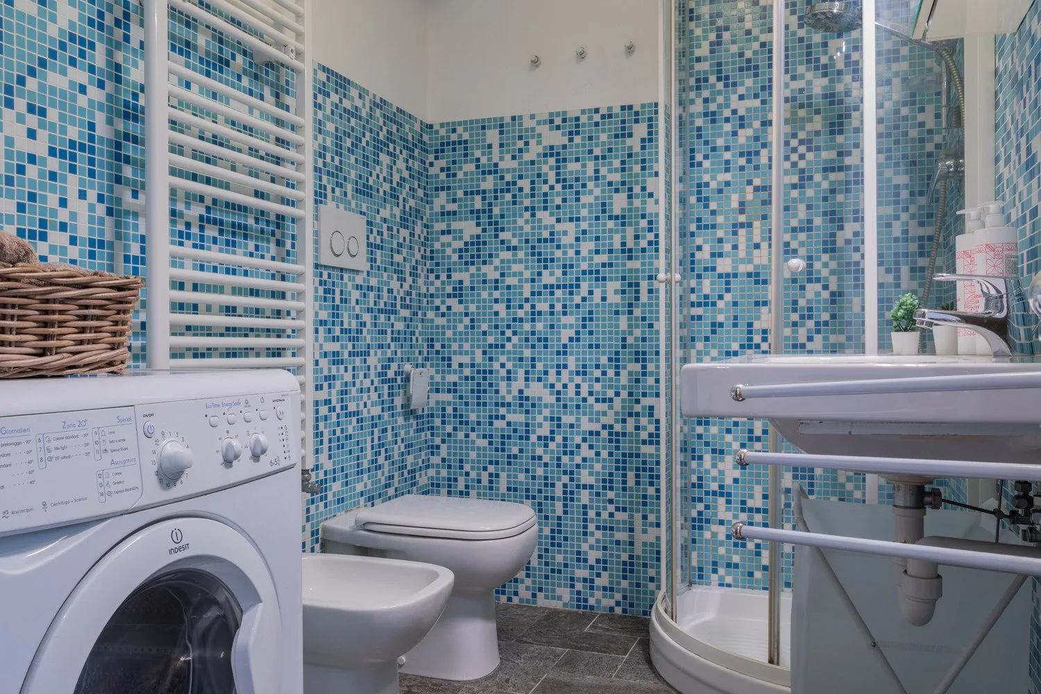Un baño alicatado con inodoro, lavabo, lavadora y ducha de cristal.
