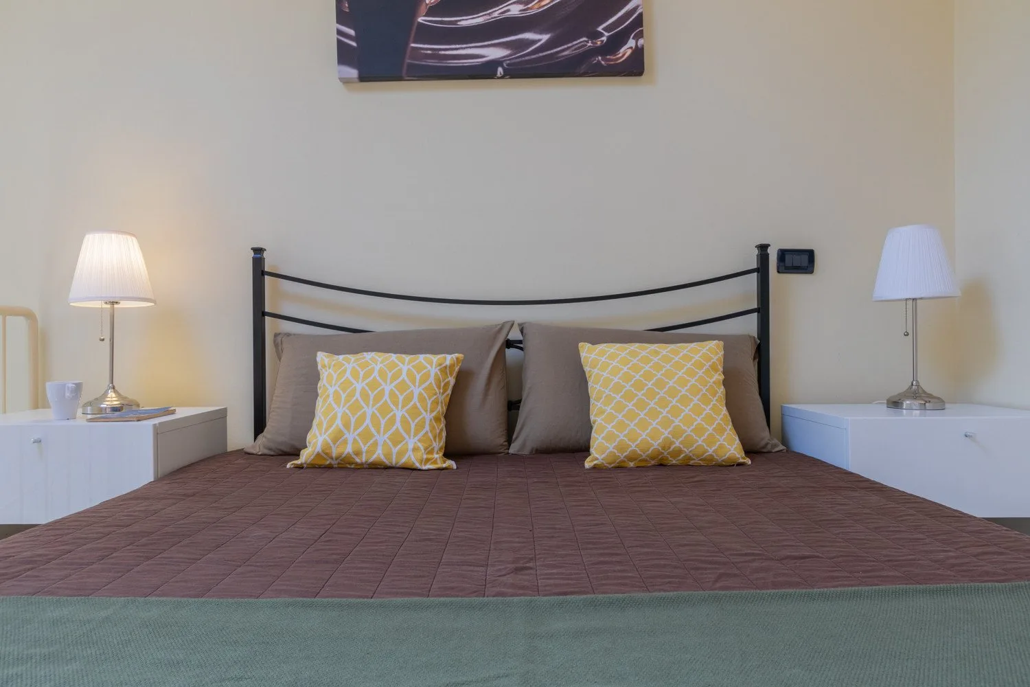 Un dormitorio con una cama, cojines decorativos amarillos y lámparas de mesilla a juego.