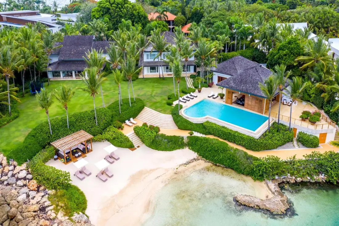 An aerial view of a tropical resort with a pool beside a sandy beach.