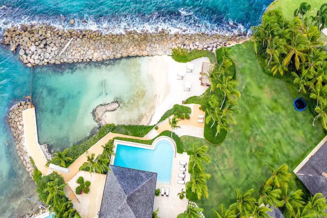 An aerial view of a resort pool beside a sandy beach and turquoise water.
