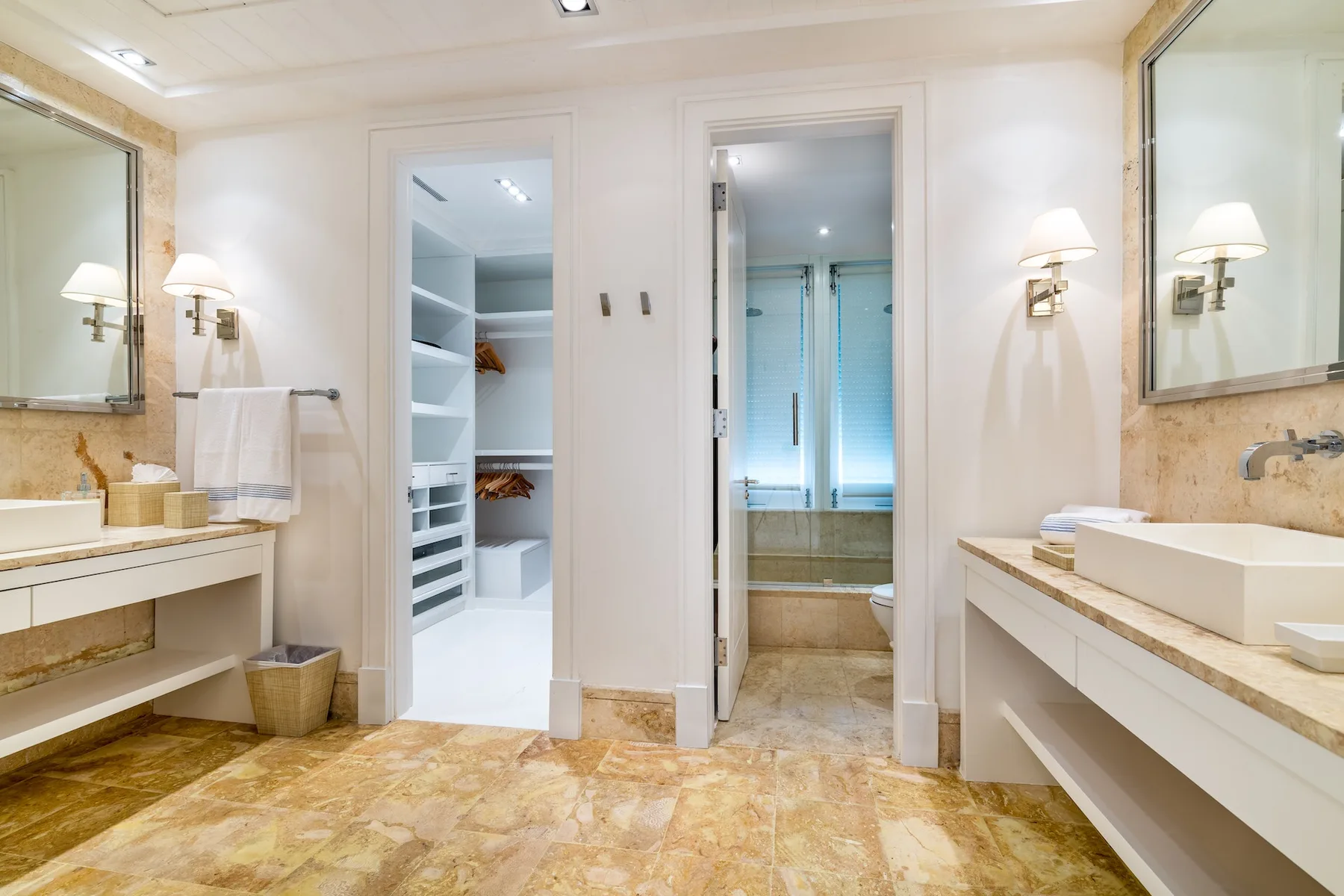 A bright bathroom with a double vanity and an open doorway to a shower.