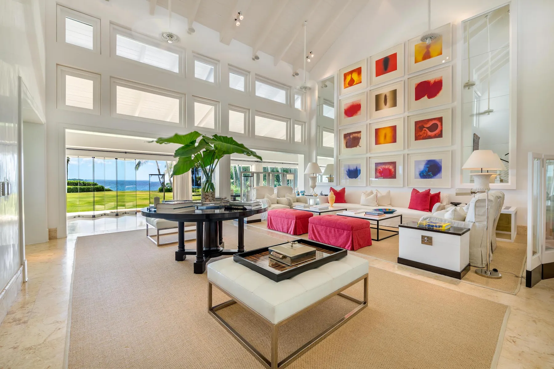 A bright living room with large windows, colorful artwork, and seating around a coffee table.