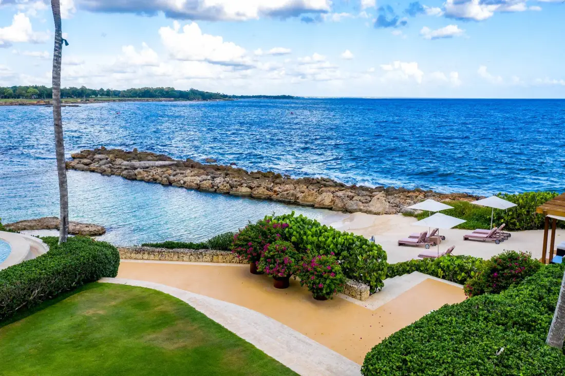 A landscaped waterfront patio overlooks a rocky shoreline and blue water.