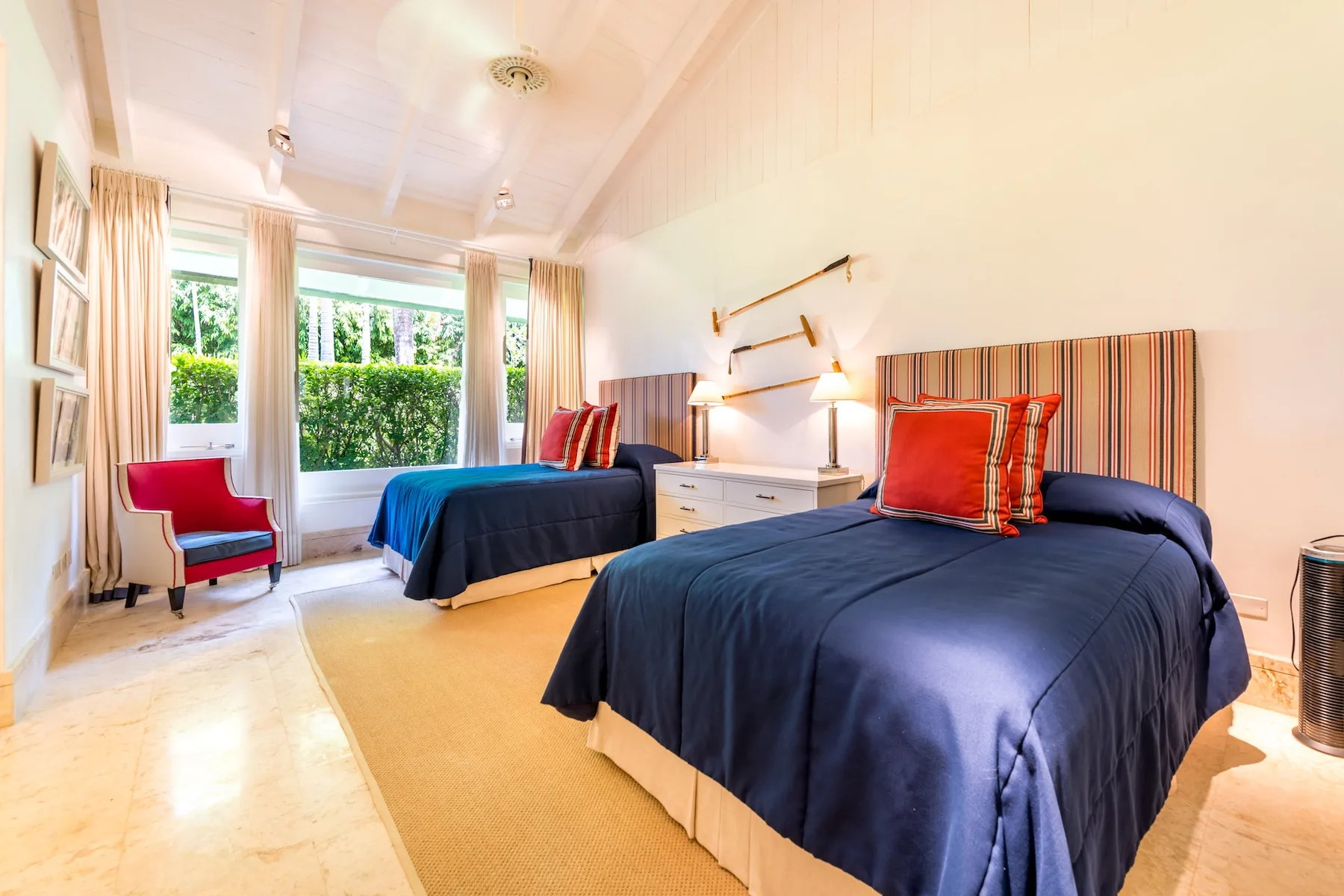 A bright bedroom with two beds, navy bedding, and large windows.