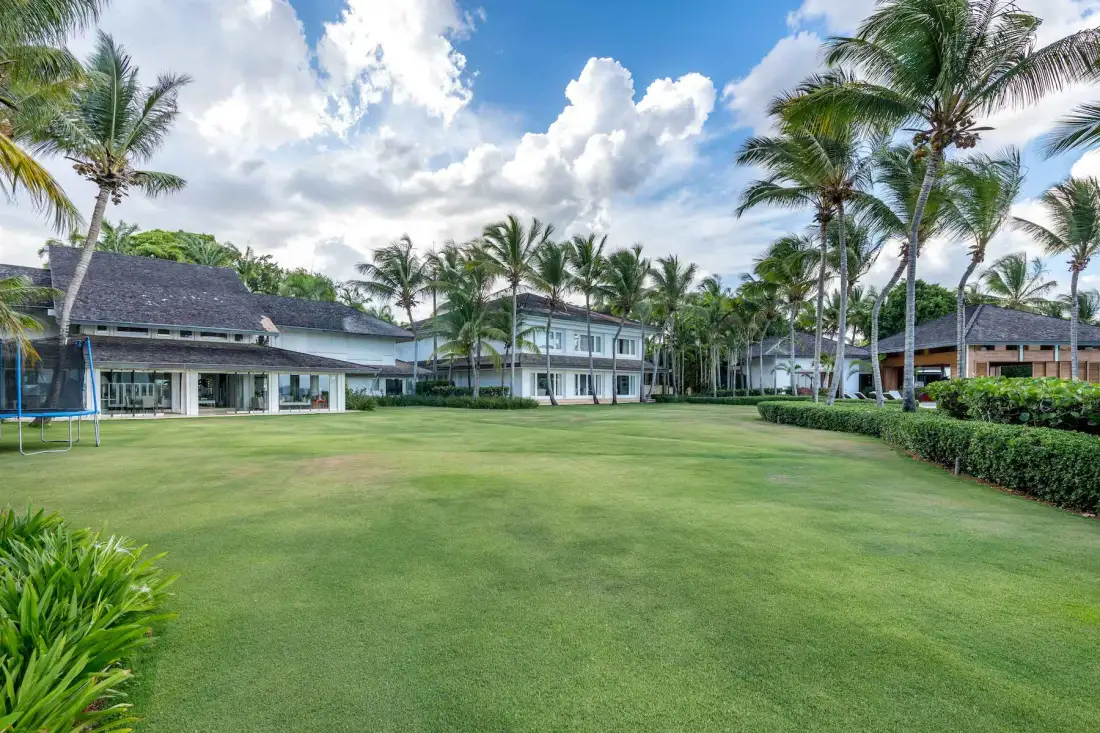 A broad green lawn stretches toward several buildings and palm trees.