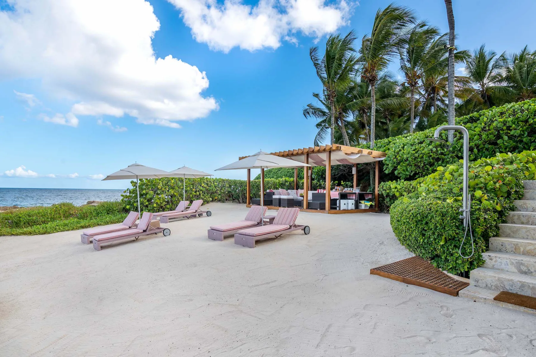 A beachfront patio with lounge seating, umbrellas, and a small open-sided bar.