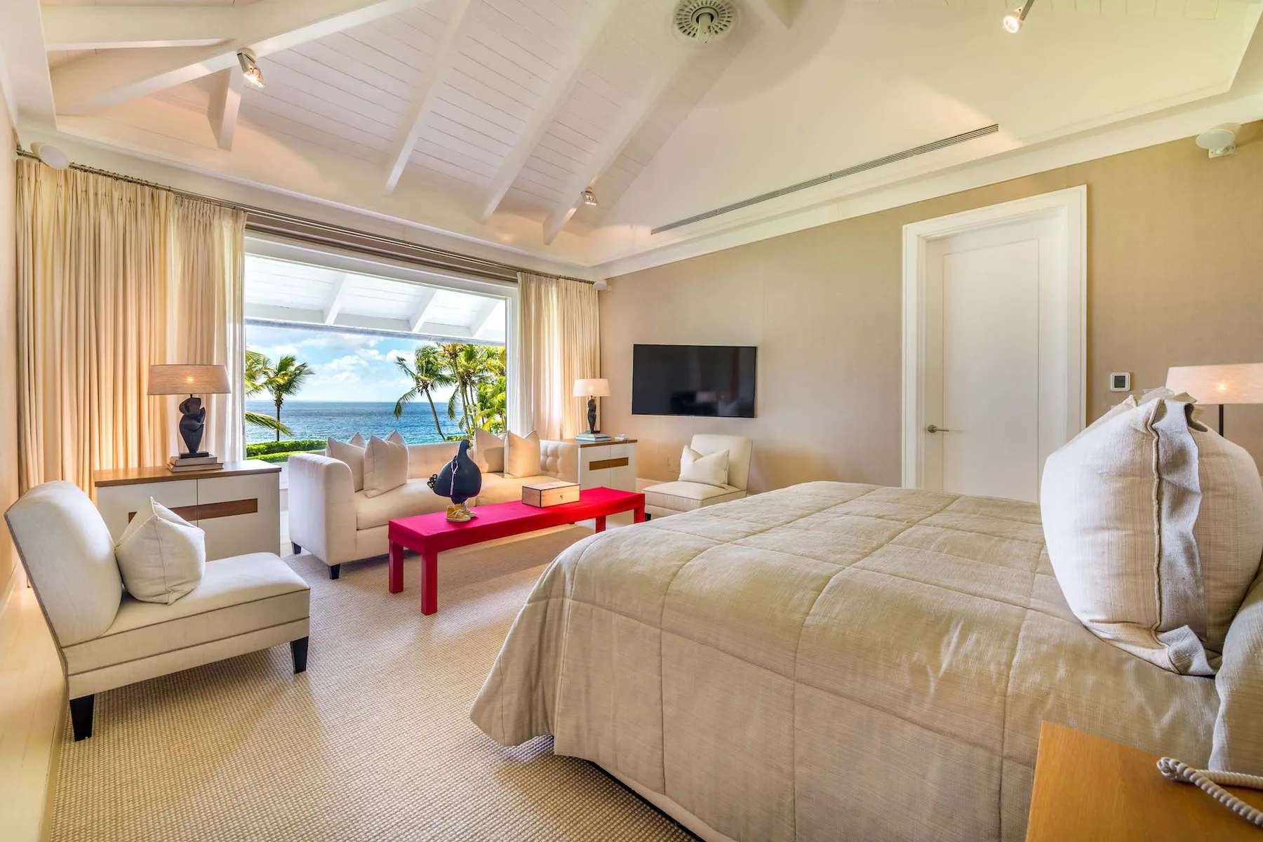 A bright bedroom with a large bed, seating area, and ocean views through the window.