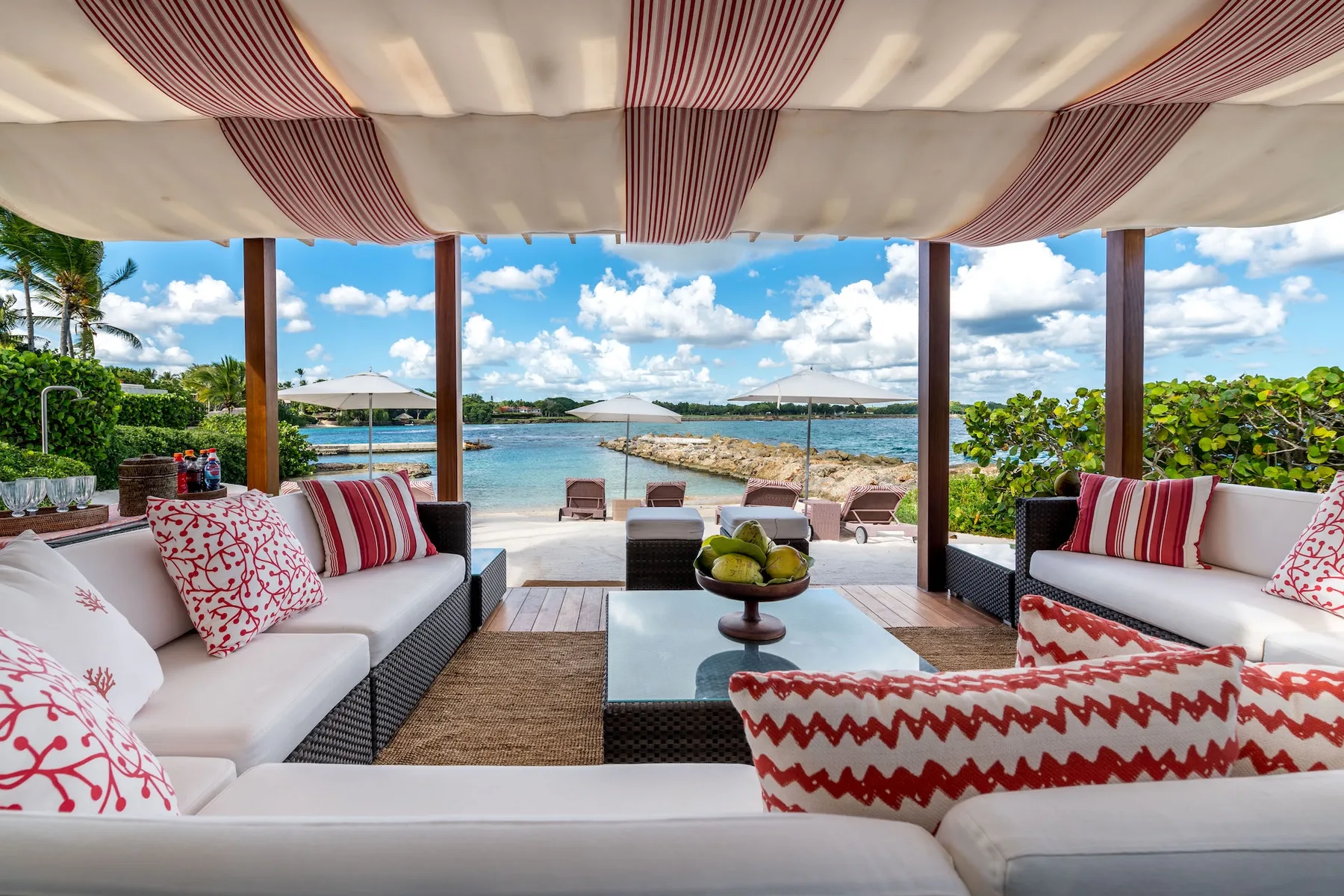 An outdoor lounge with cushioned seating overlooks the water beneath a striped canopy.