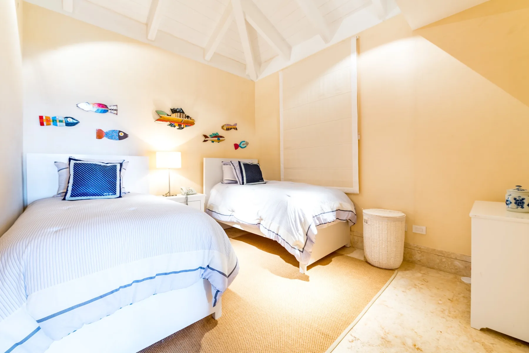 A bright bedroom with two beds beneath a white vaulted ceiling.