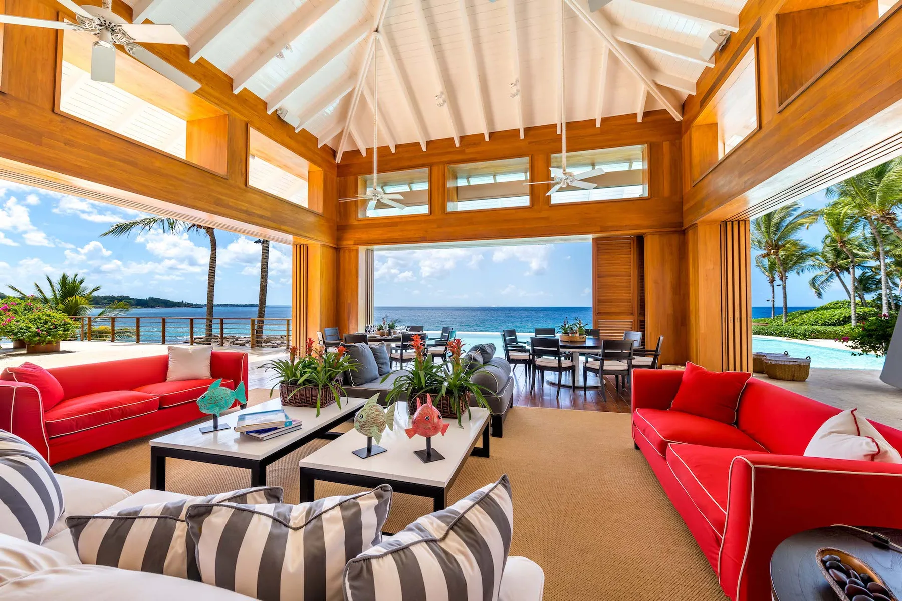 An open living room with red seating and a dining area facing the ocean.