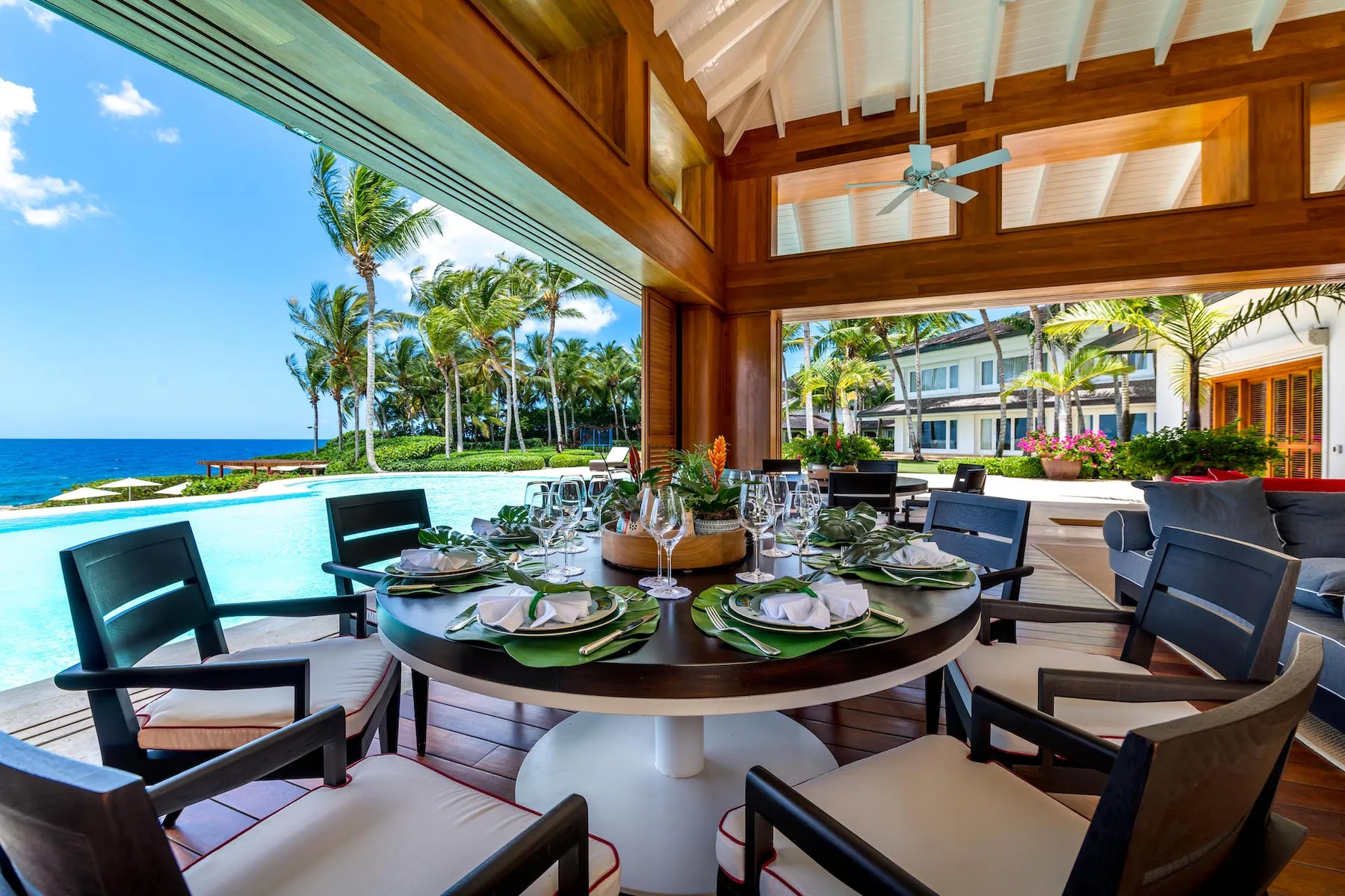 An open-air dining area with a set table overlooking a pool and ocean.