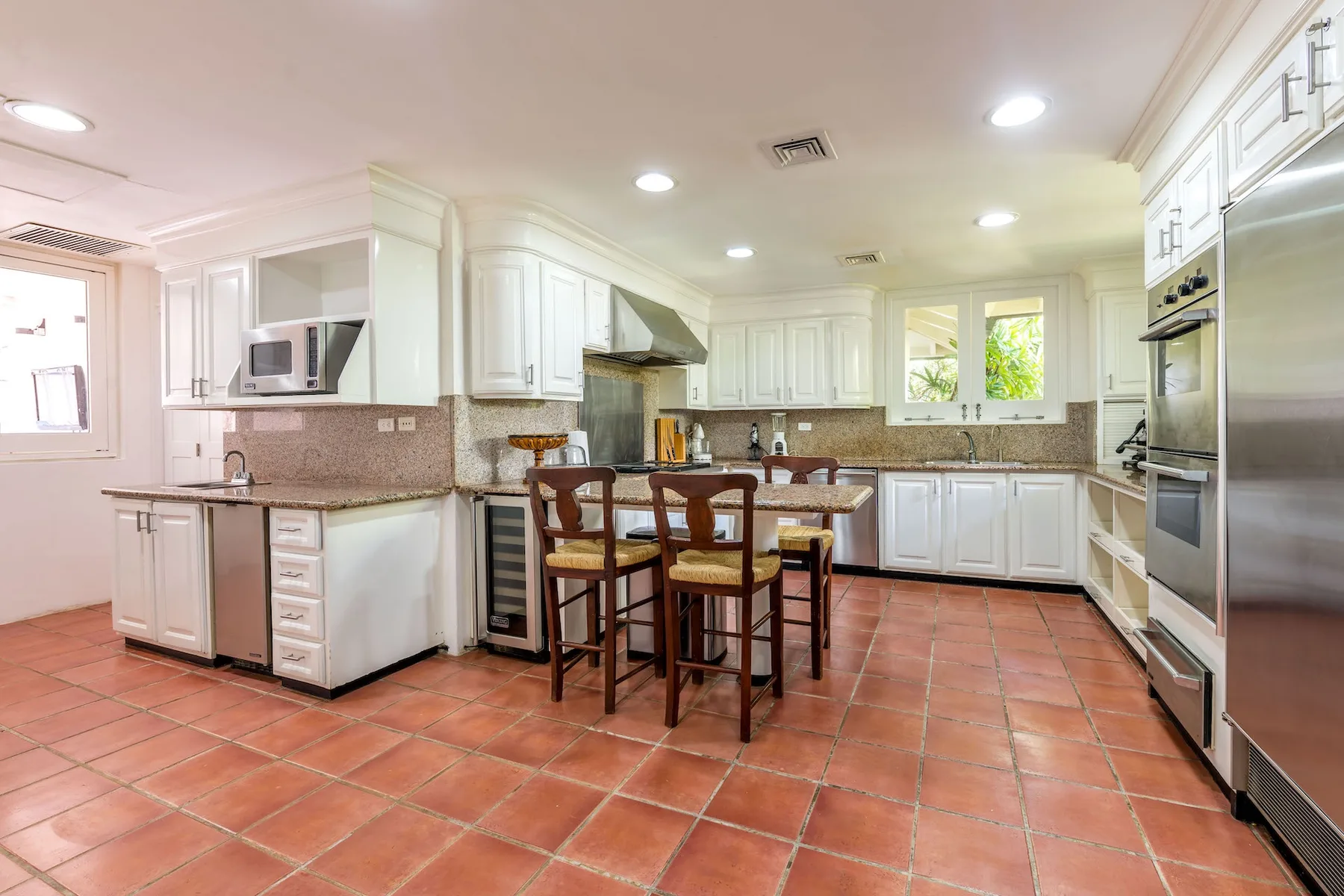 A bright kitchen with white cabinets, tiled floors, and a central island with seating.