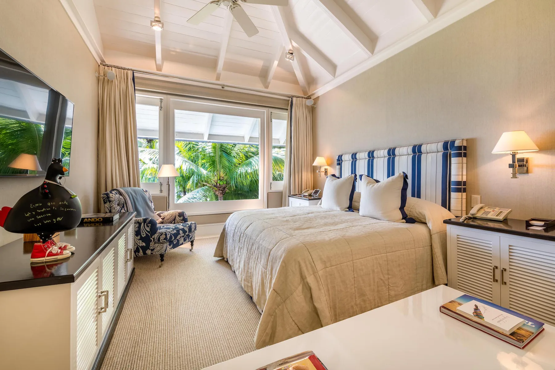 A bedroom with a large bed and windows overlooking tropical greenery.