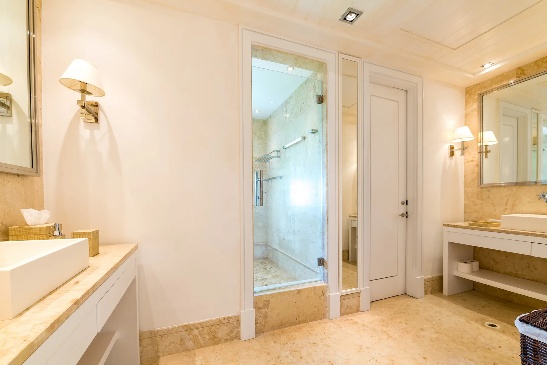 A bright bathroom with a glass shower and vanity sinks.