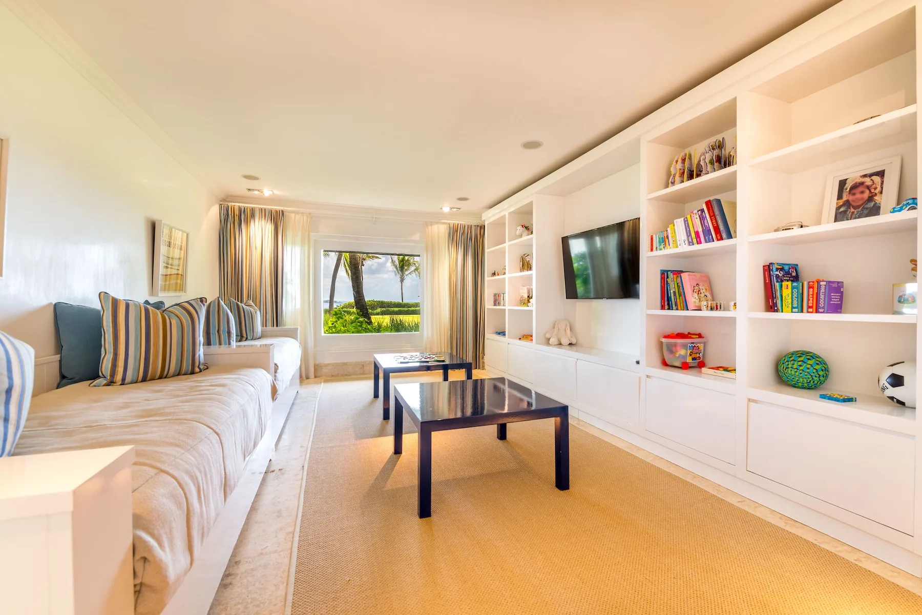 A bright living room with seating, a television, bookshelves, and coffee tables.