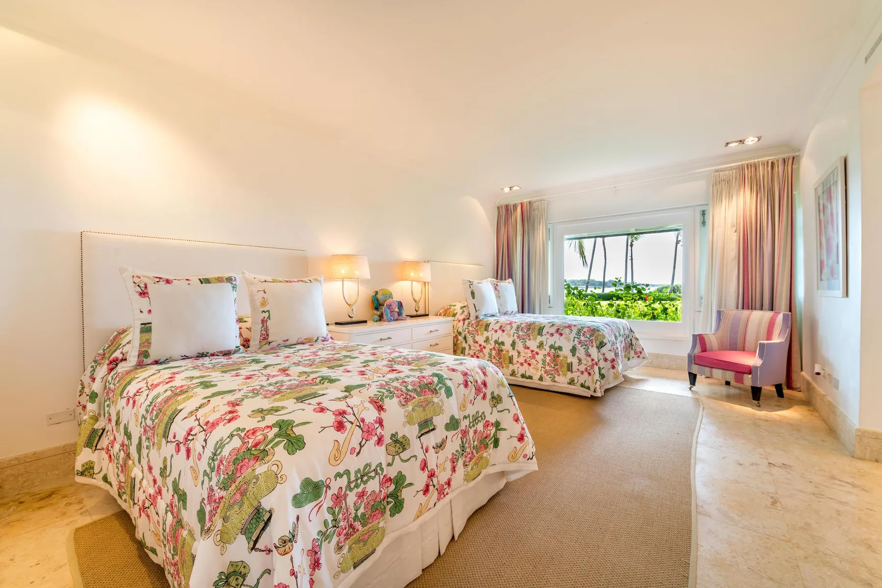A bright bedroom with floral bedding, a second bed, and a window overlooking greenery.