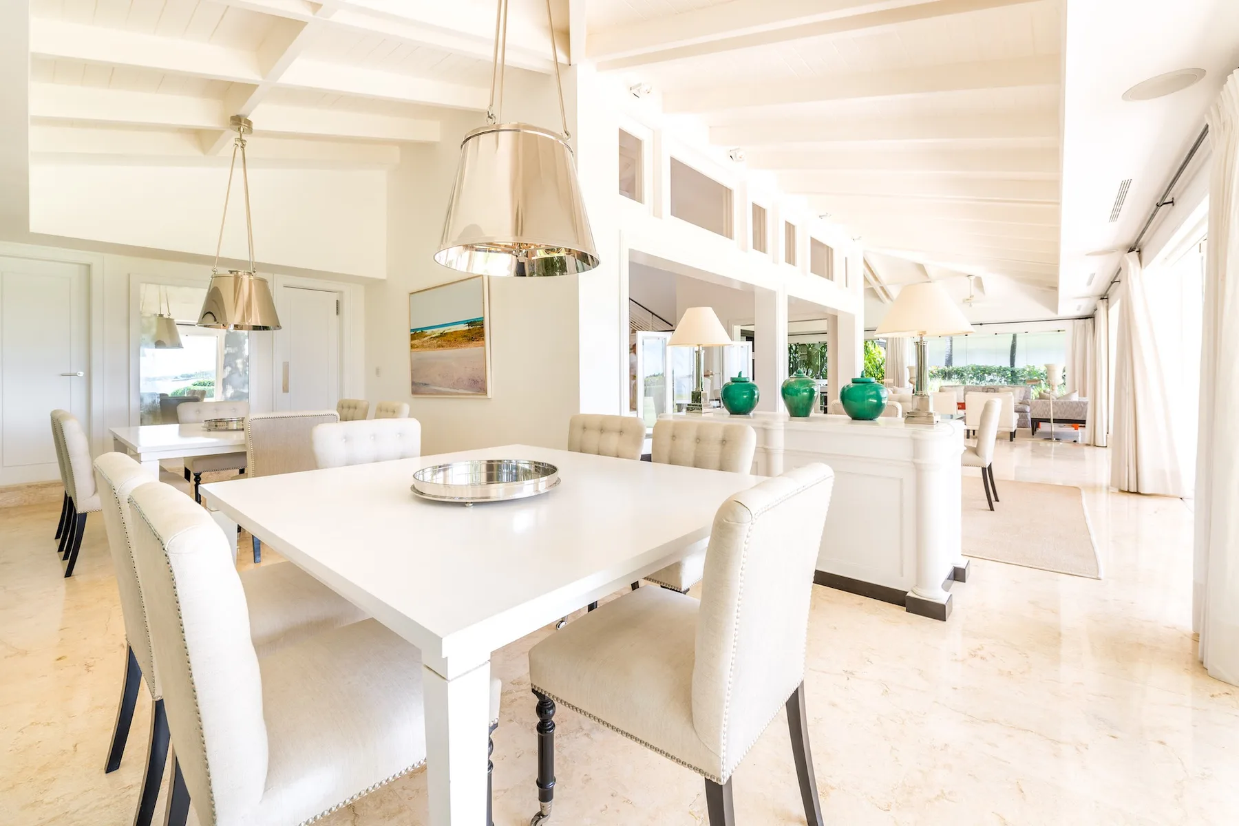 A bright dining area with a long table and a kitchen island behind it.