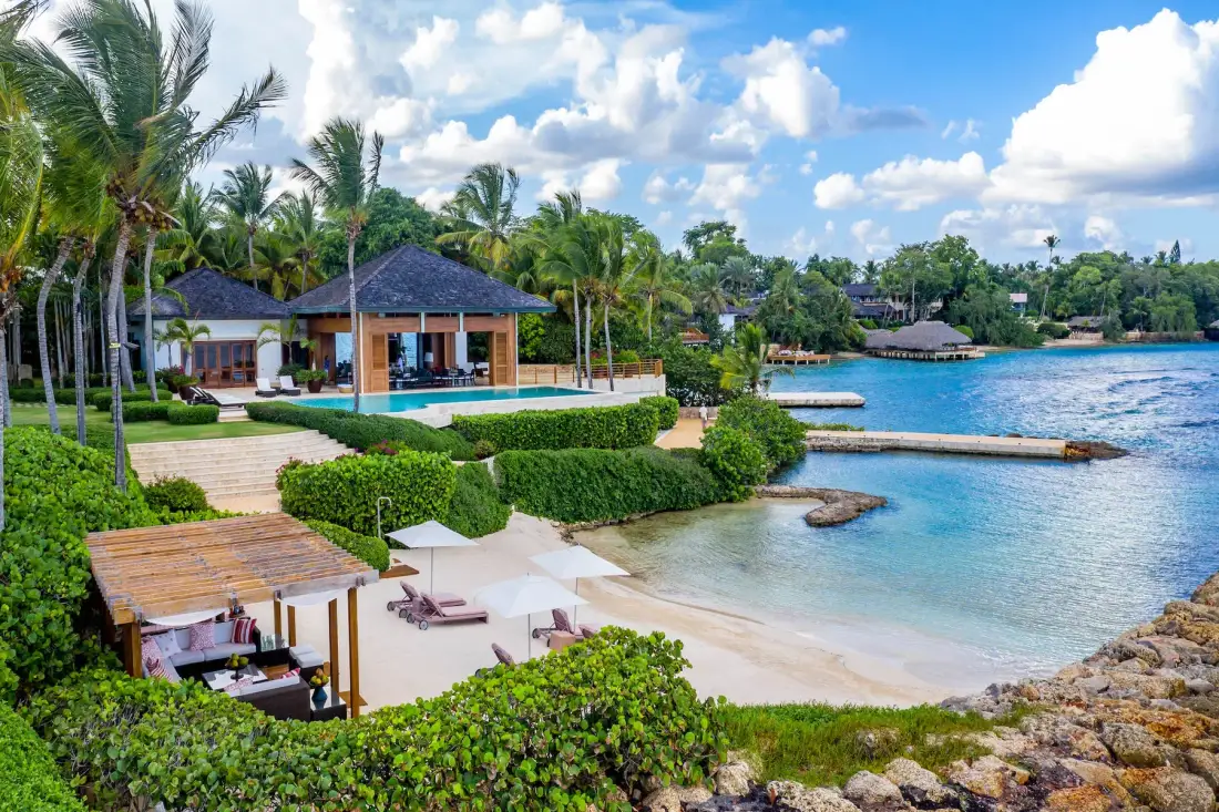 A tropical beachfront resort with a pool, sandy shore, and lush palms.