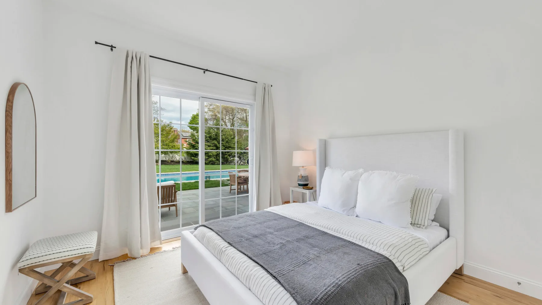 A bright bedroom with a white bed beside a large window.