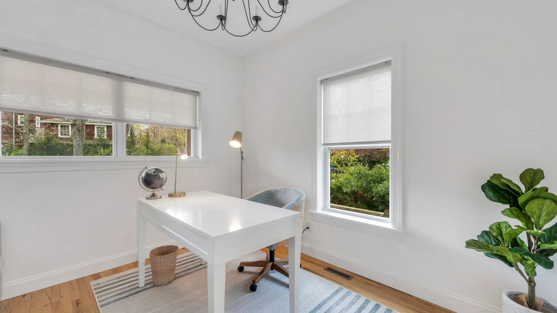 A bright home office with a white desk, a window, and a leafy plant.