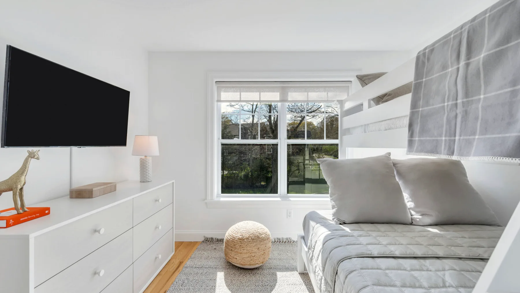 A bright bedroom with a bed, white dresser, and large window.