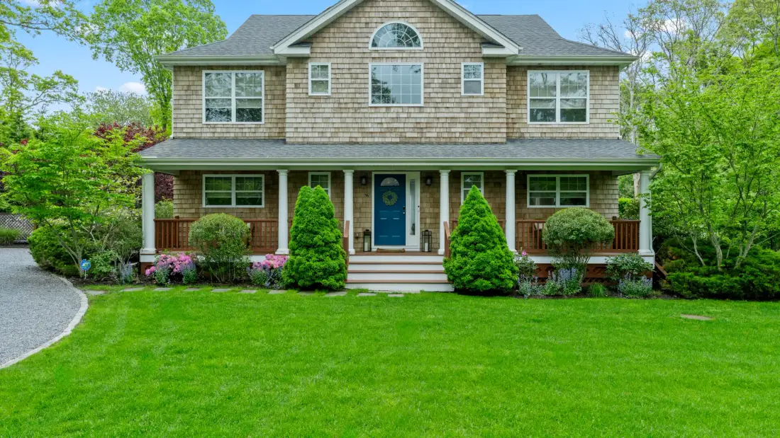 A two-story house with a covered front porch stands behind a green lawn.