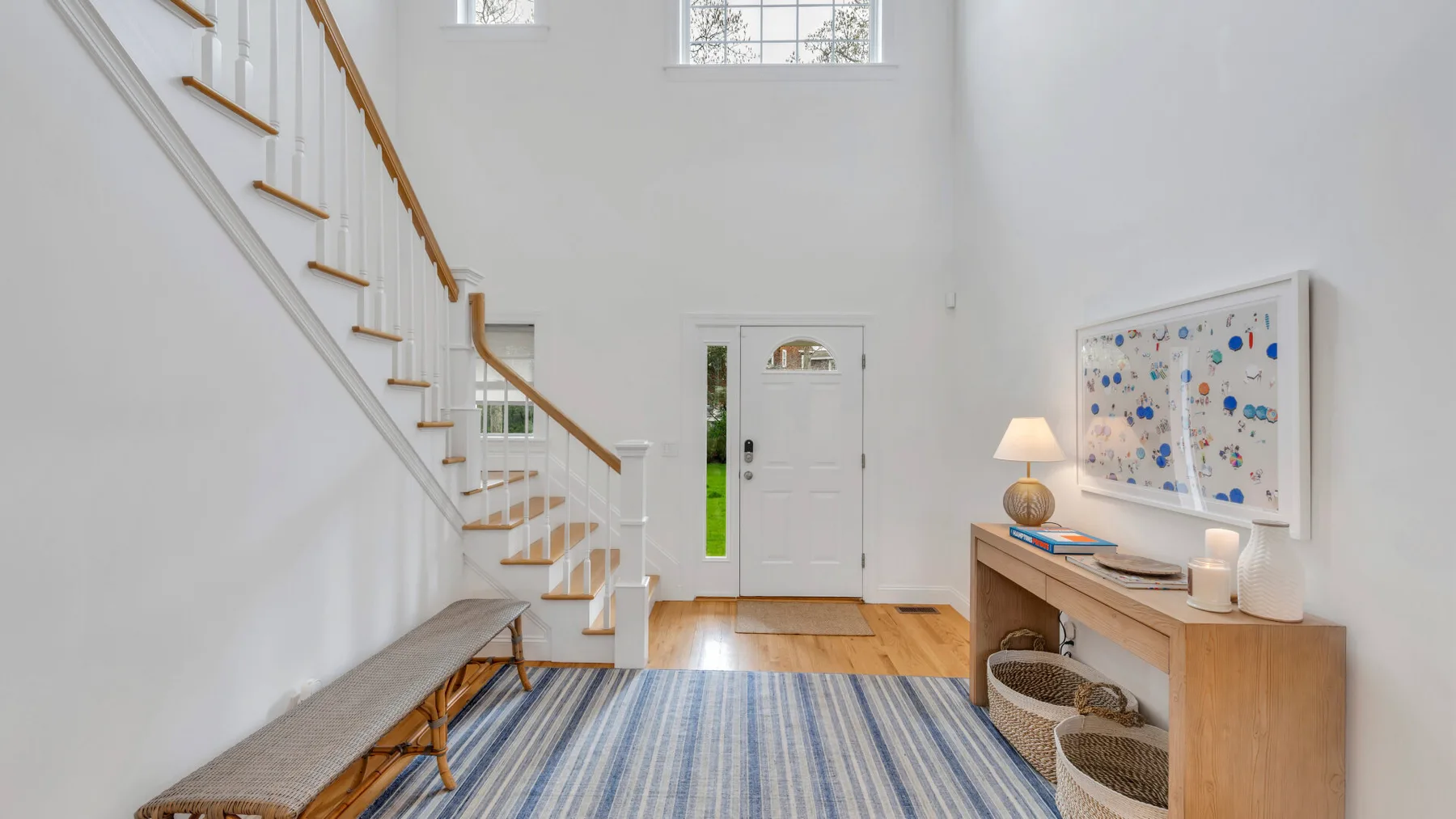 A bright entryway with a staircase, striped rug, and wooden console.