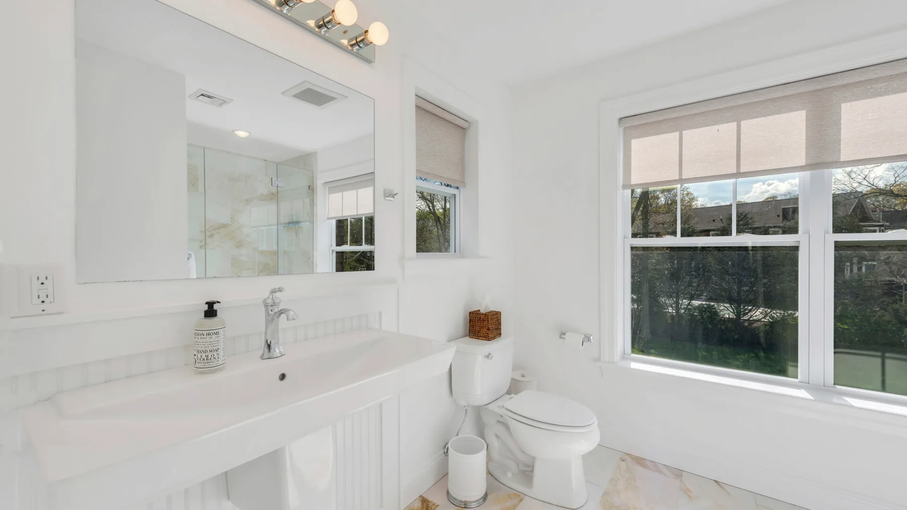 A bright bathroom with a long vanity, mirror, and large window.