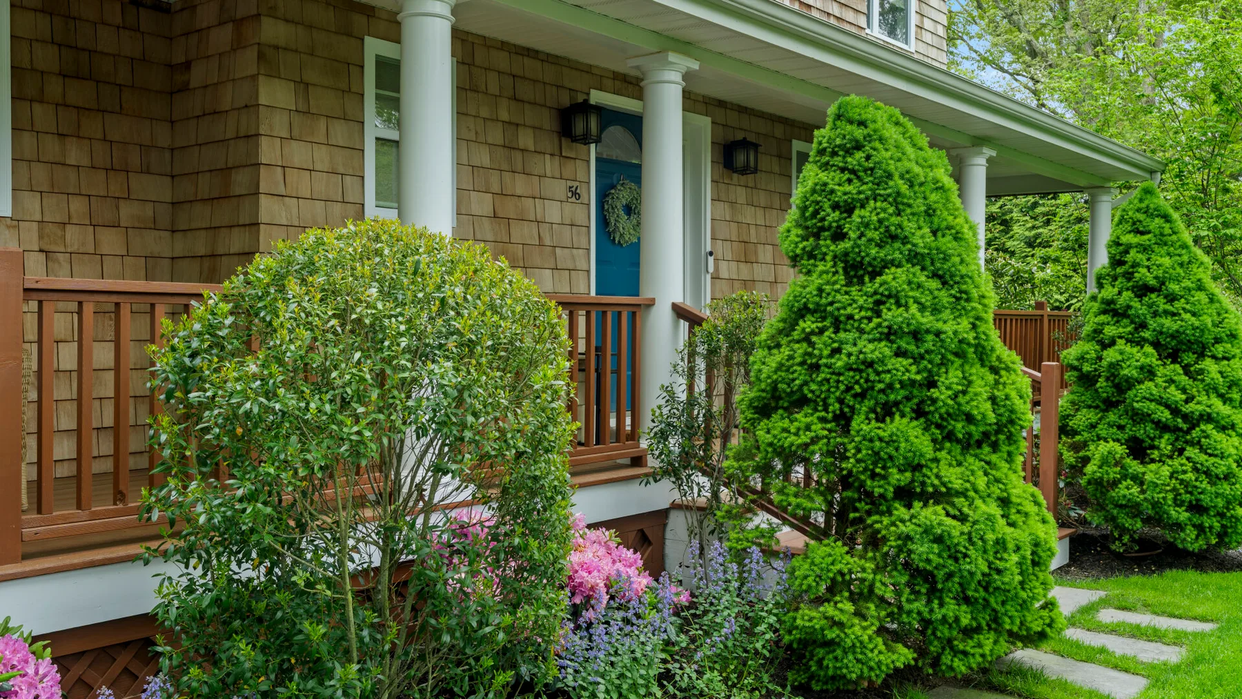A house entrance with a wooden porch railing and landscaped shrubs.