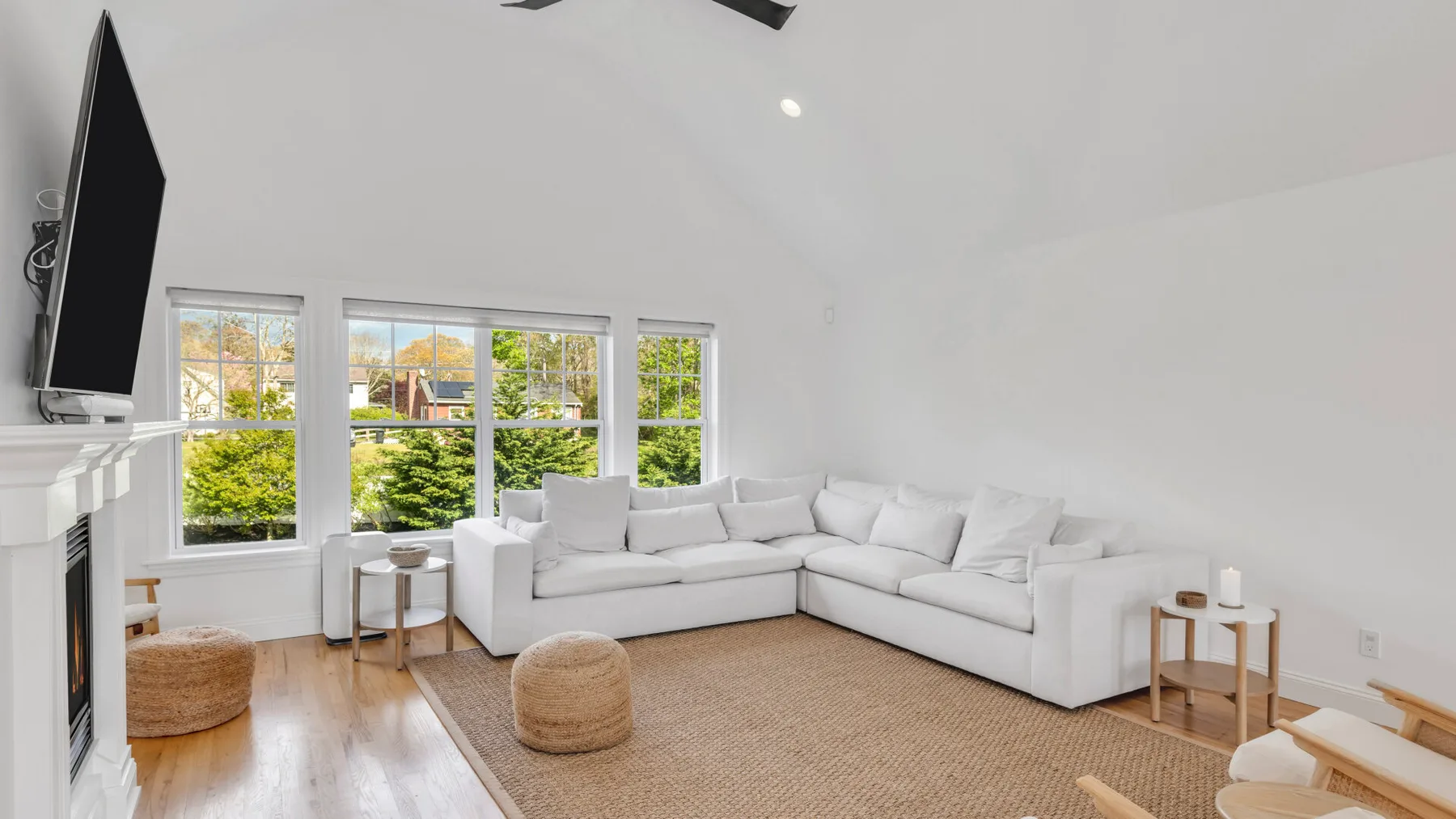 A bright living room with white seating, large windows, and a woven rug.