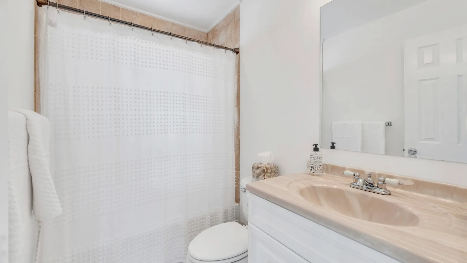A bathroom with a sink, mirror, and curtained shower.