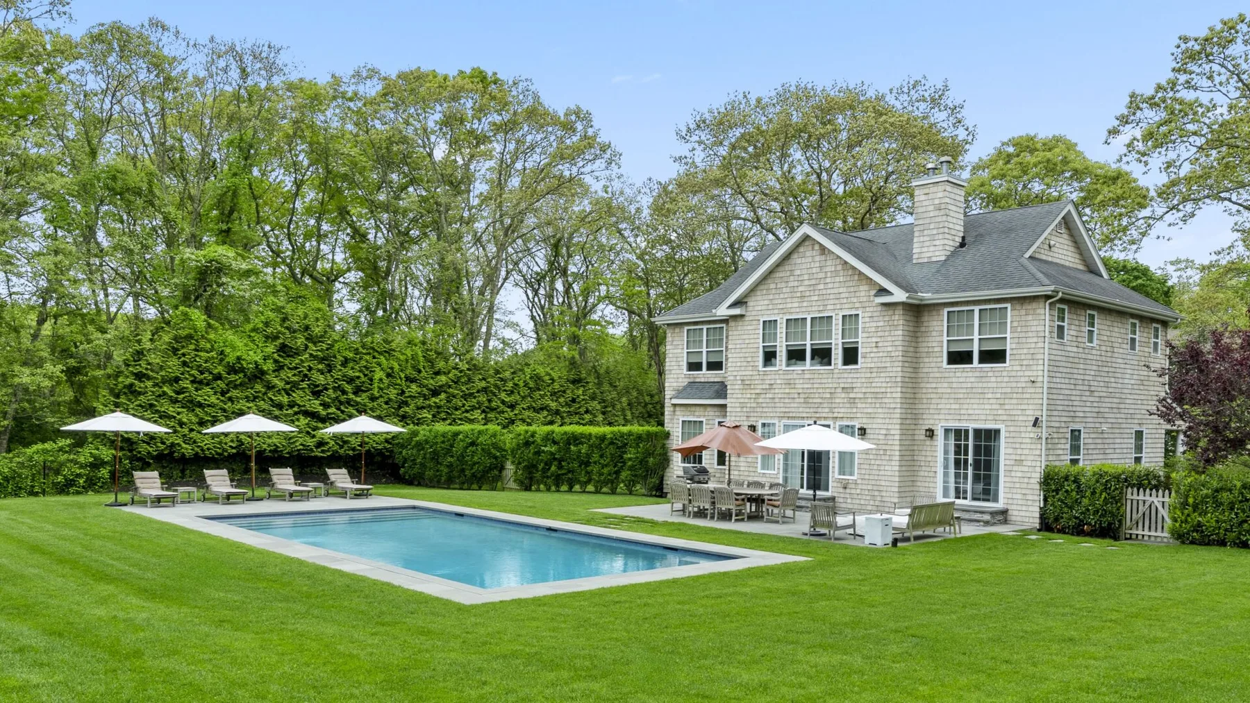 A landscaped yard with a swimming pool and a two-story house.