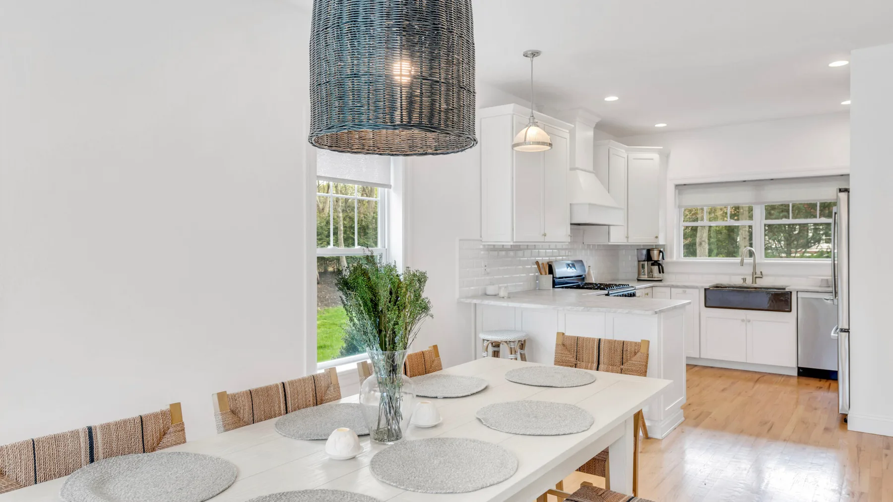 A bright open kitchen and dining area with a white table and leafy greenery.