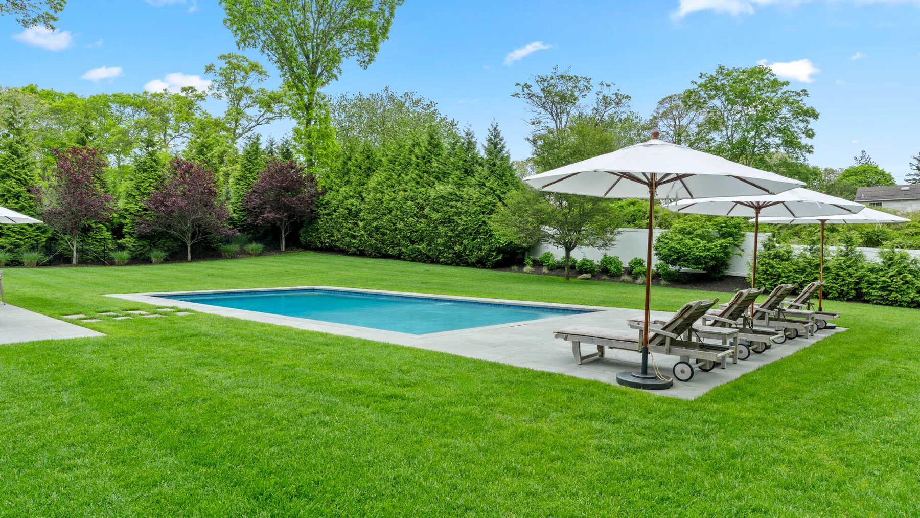 An outdoor swimming pool sits beside a grassy lawn, with loungers under umbrellas.