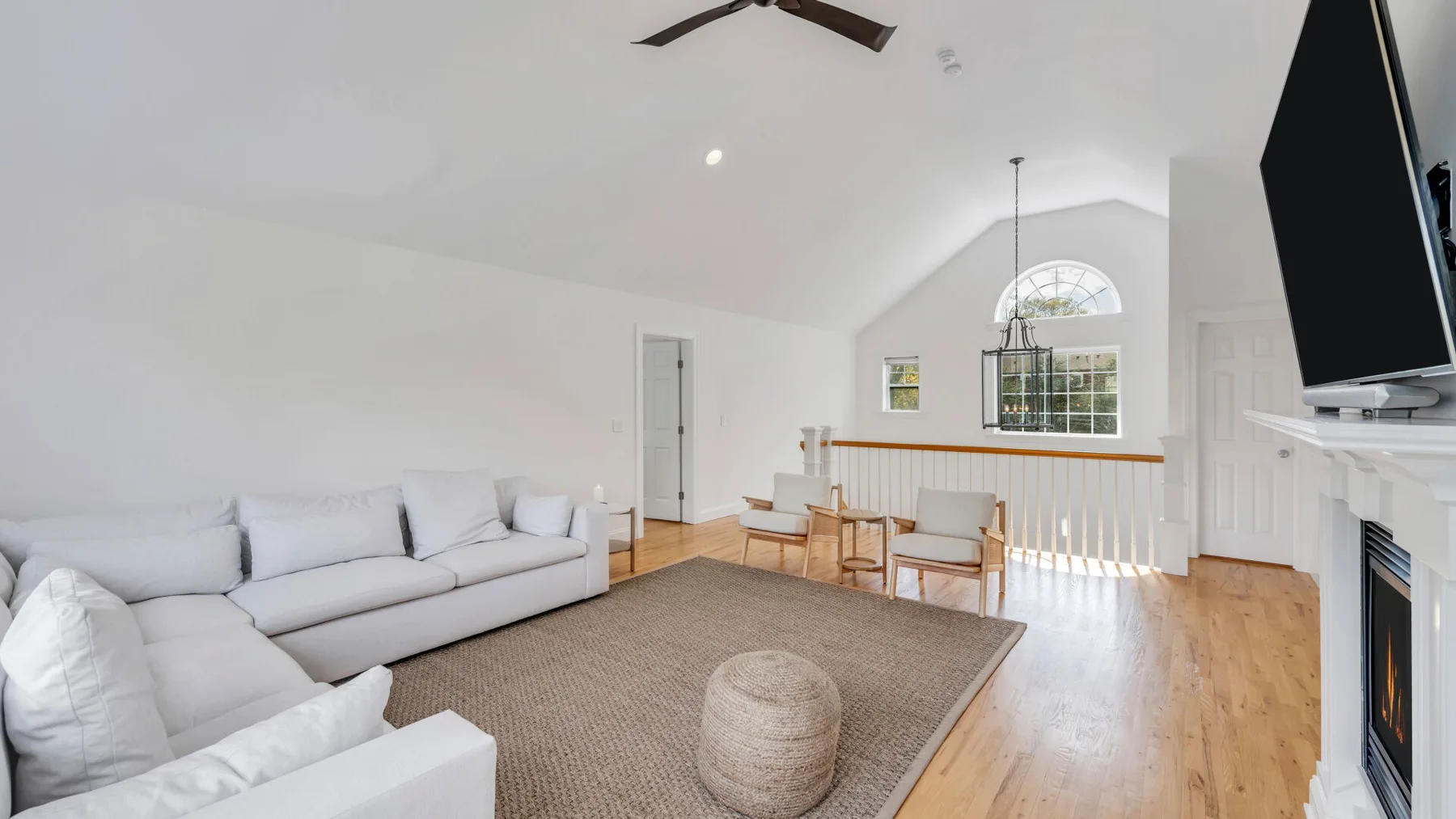 A bright living room with seating, a rug, and a dining table beneath high windows.