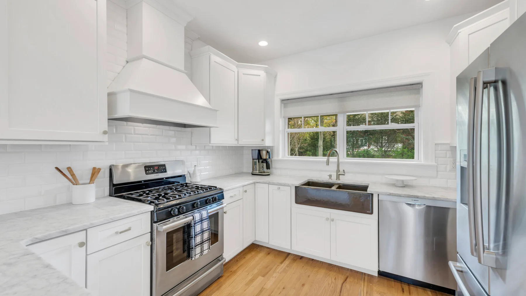 A bright white kitchen with a gas range, sink, and stainless steel appliances.
