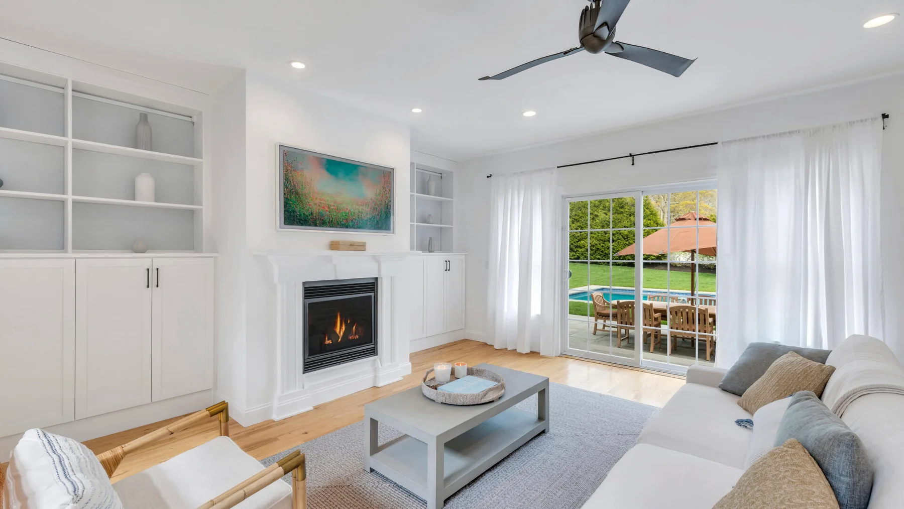 A bright living room with seating, a coffee table, and glass doors opening to a garden.
