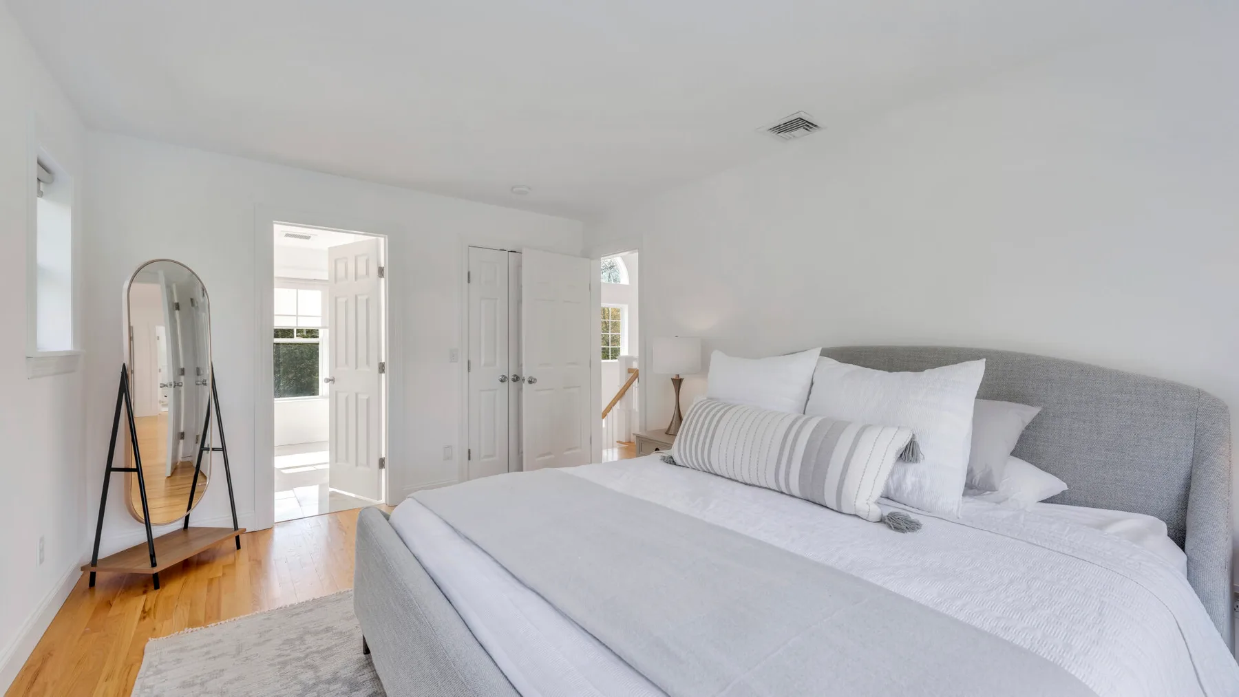 A bright bedroom with a neatly made bed and gray upholstered headboard.