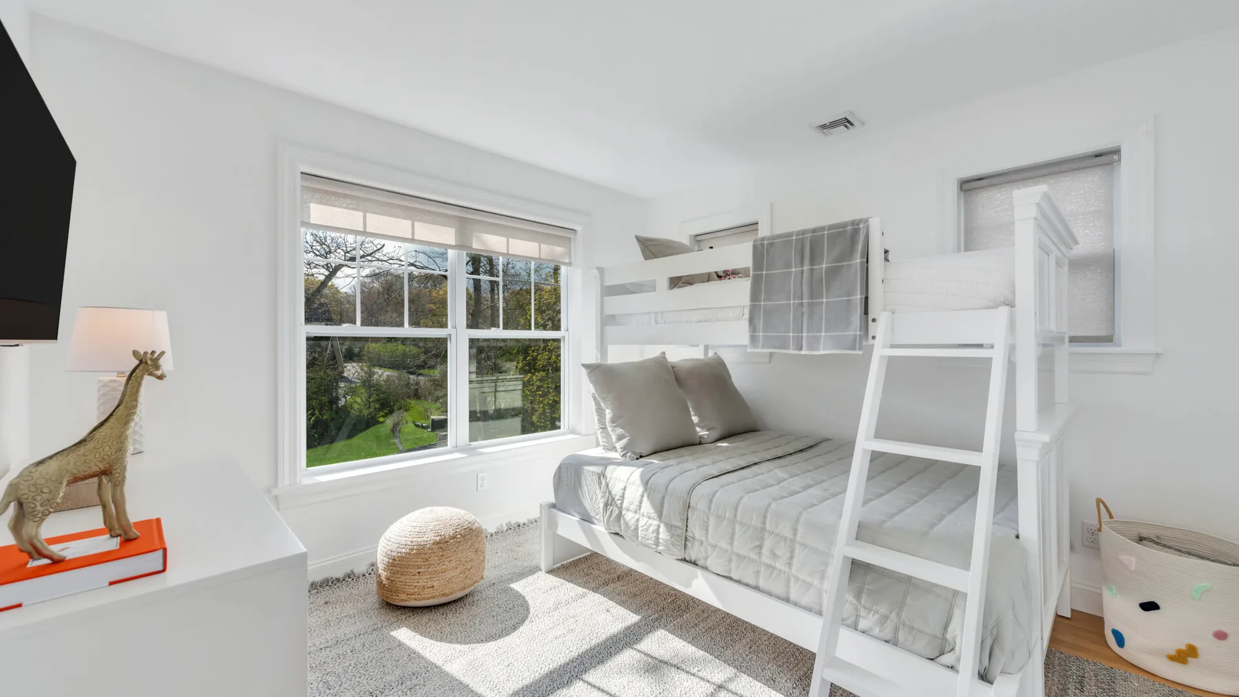 A bright bedroom with a bunk bed and large windows overlooking greenery.