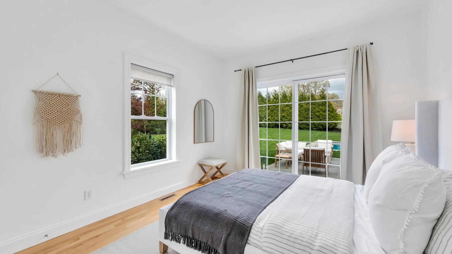 A bright bedroom with a bed beside large windows overlooking greenery.