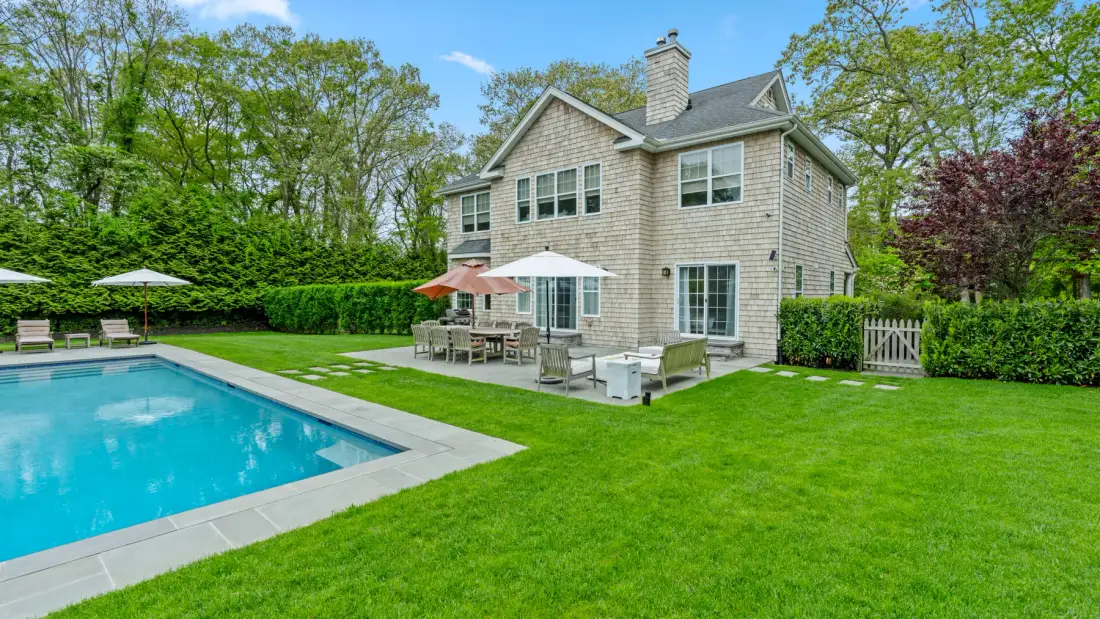 A house stands beside a swimming pool and a green lawn.