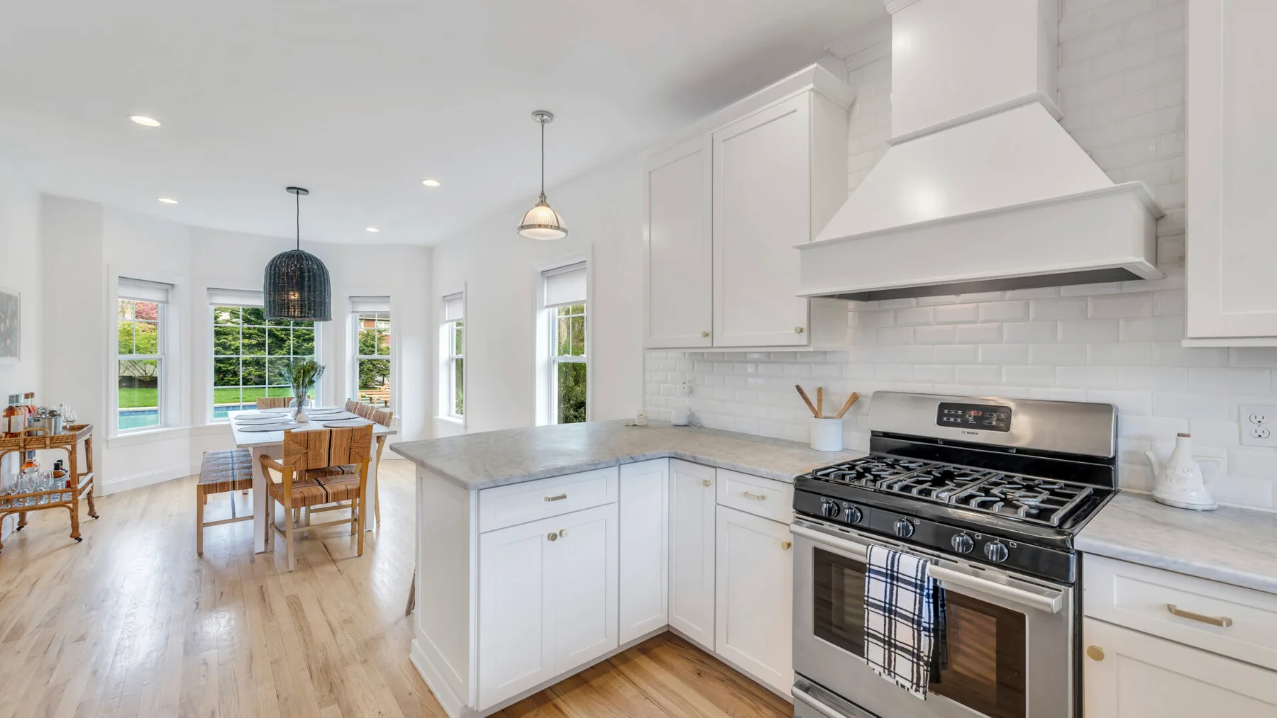 A bright kitchen opens onto a dining area, with white cabinetry and a large range.