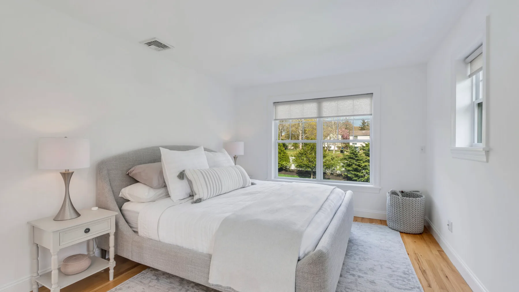 A bright bedroom with a neatly made bed and large windows overlooking greenery.