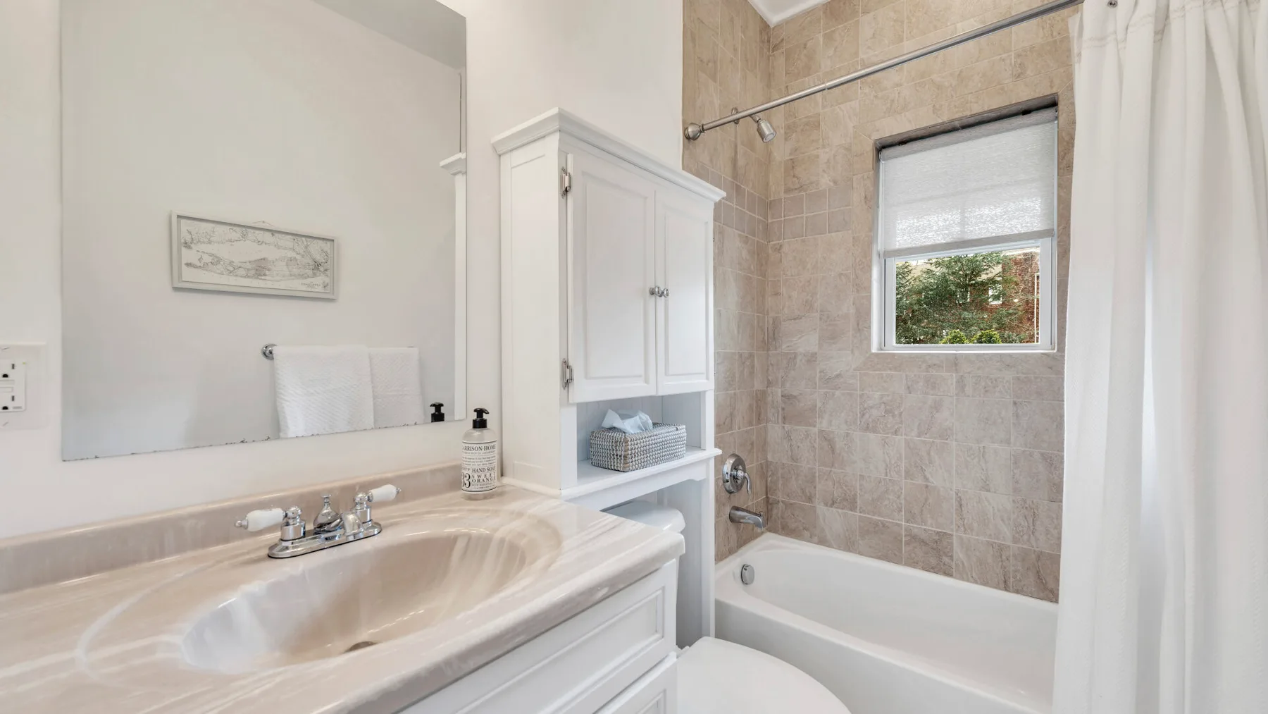 A bright bathroom with a sink, mirror, and bathtub beside a window.