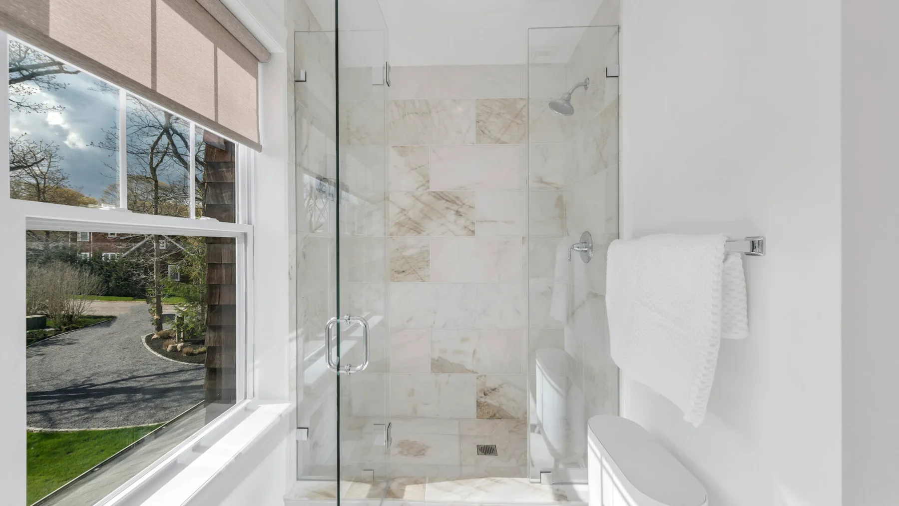 A bathroom with a glass shower beside a large window.