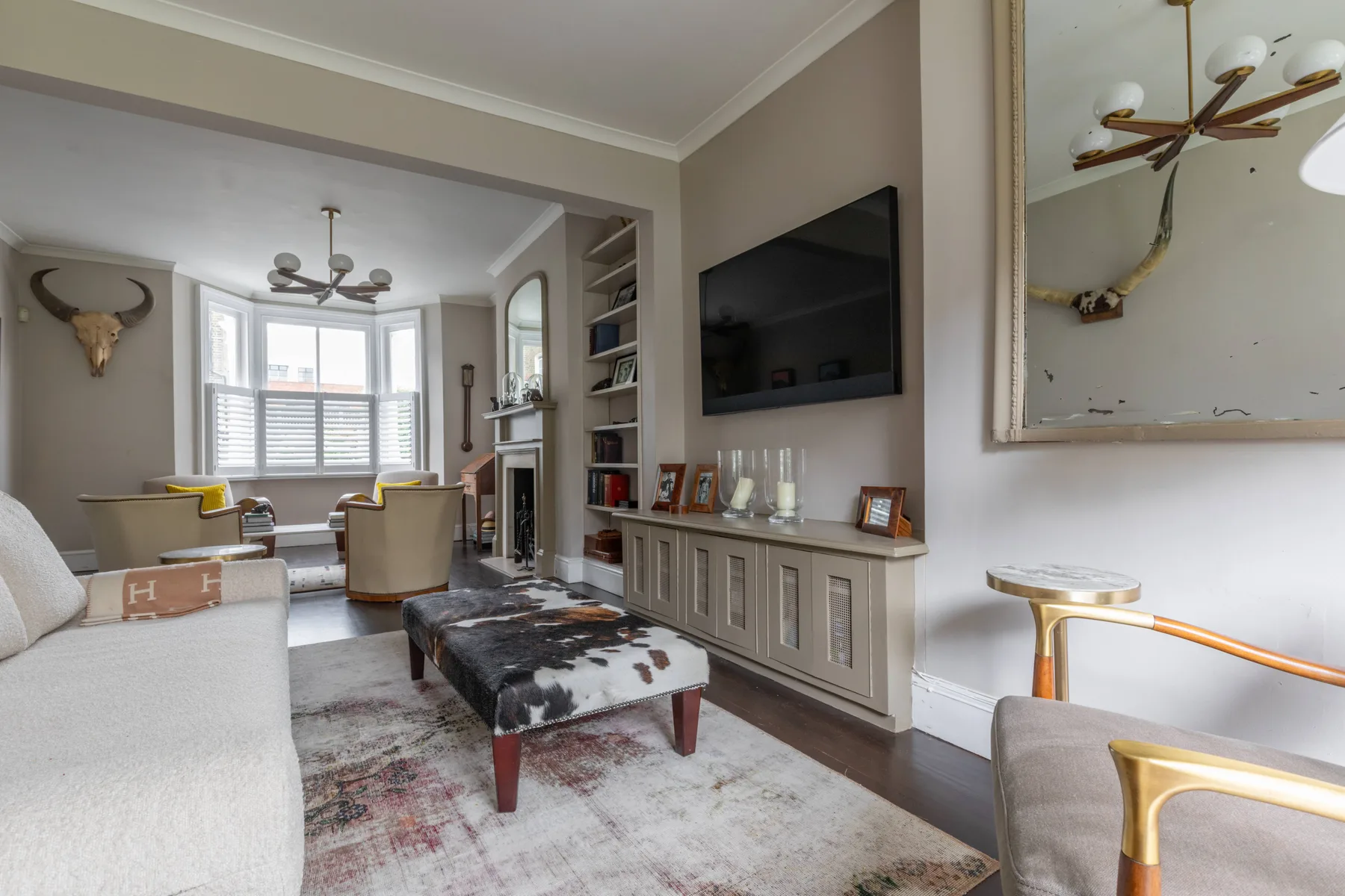 Una sala de estar con un televisor sobre un mueble empotrado y asientos junto a las ventanas.