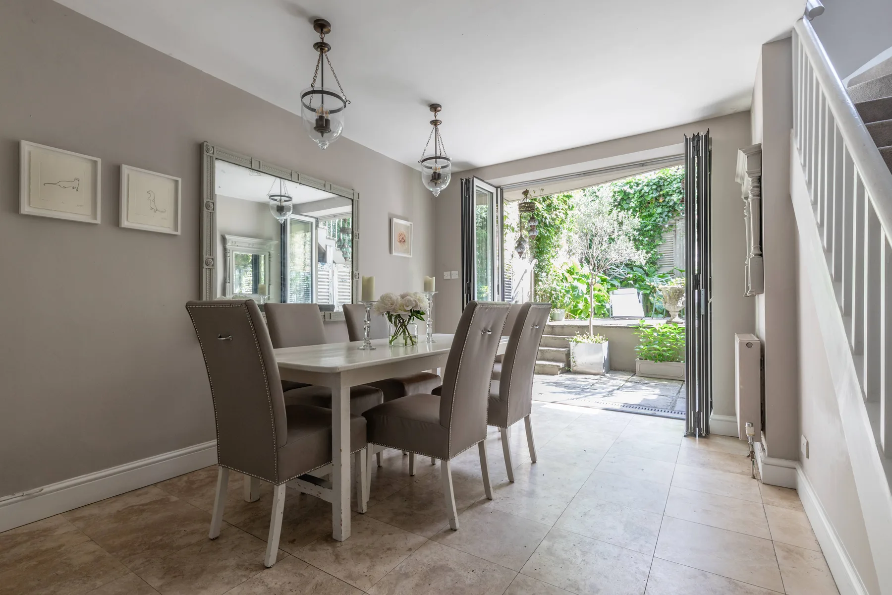 Dining area with a table and chairs beside open doors to a garden.